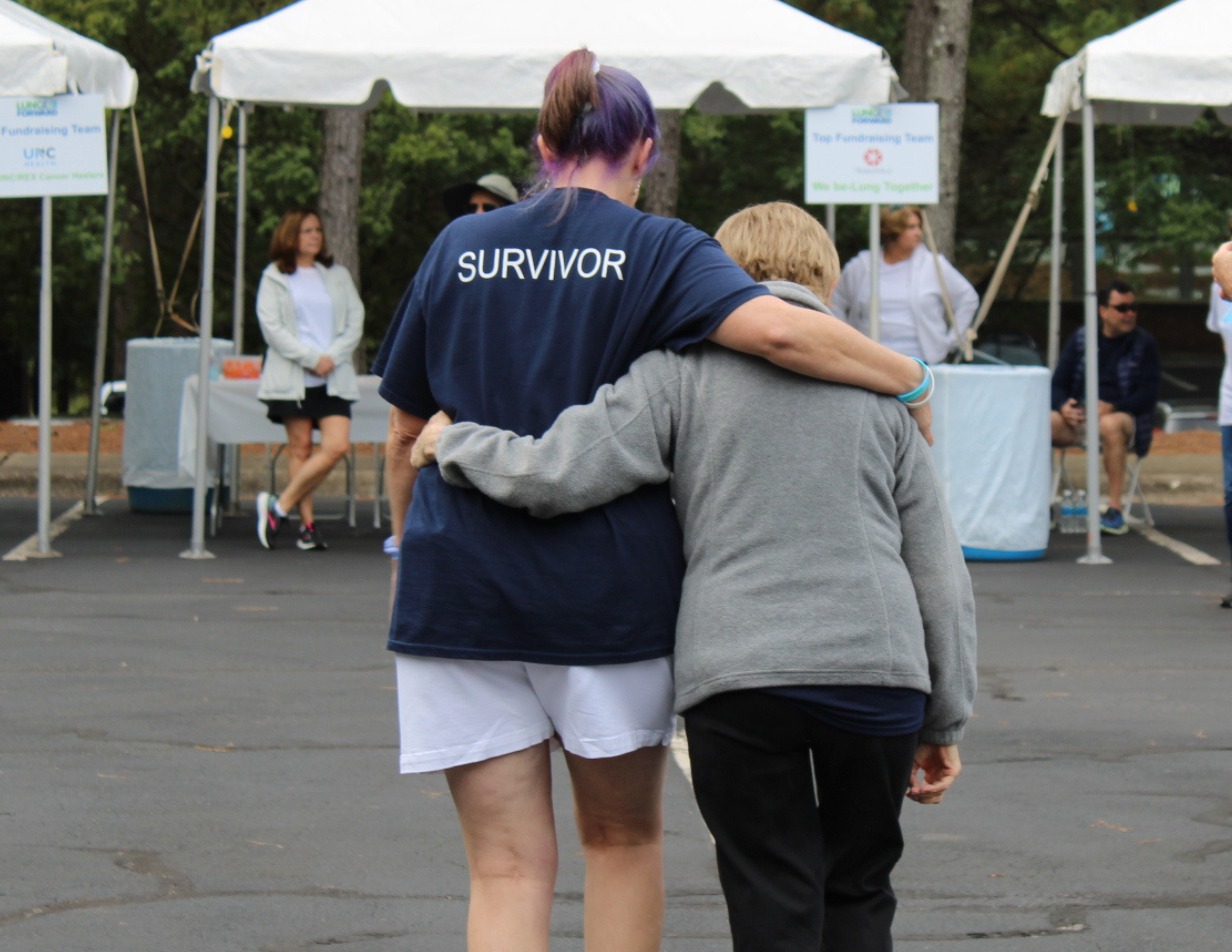 A lung cancer survivor in a navy Survivor shirt walks arm in arm with a companion at a community walk event