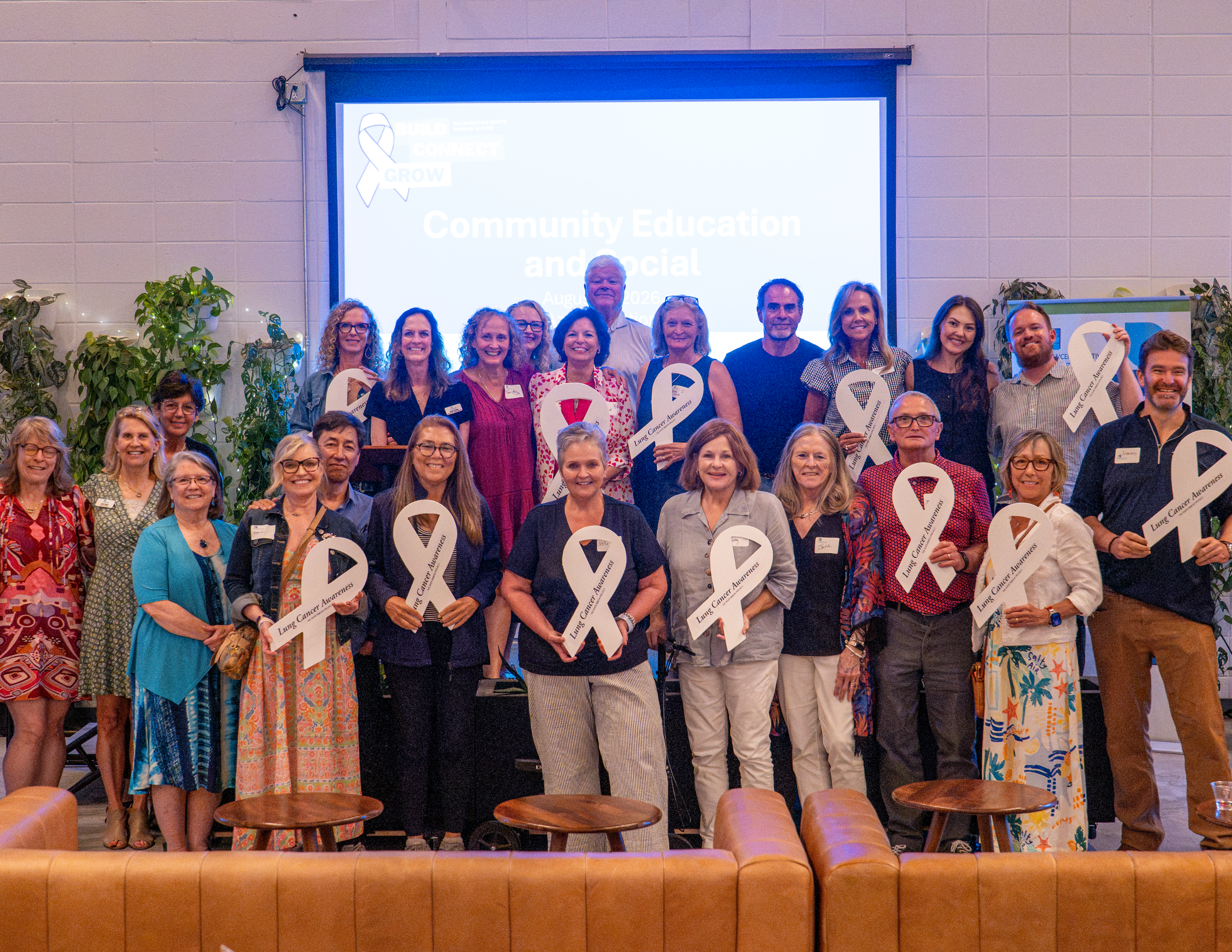 Community members smiling and holding white Lung Cancer Awareness ribbons at a Community Education and Social event
